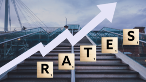 A person walking up a set of stairs, representing the challenges of rising interest rates in the UK, with relationn to mortgage rates. The text "RATES" overlays the image of the stairs with an upward arrow visually signalling the topic of rising rates